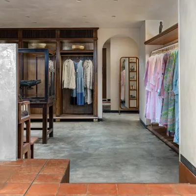 A view from the terracotta-tiled courtyard into the main retail space at Eka. The transition to a polished concrete floor marks a shift to a more intimate atmosphere, where custom wood wardrobes and antique displays showcase the clothing.
