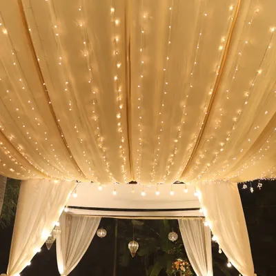 A romantic seating area under a canopy of draped fabric and warm fairy lights.