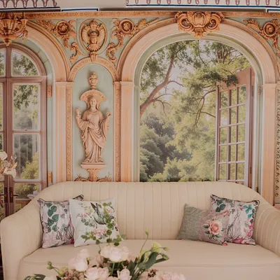 A romantic seating area from our 'Mint to Be' event. A plush cream sofa is set against a backdrop of painted French-style windows and arches, creating the illusion of being in a beautiful European garden pavilion.