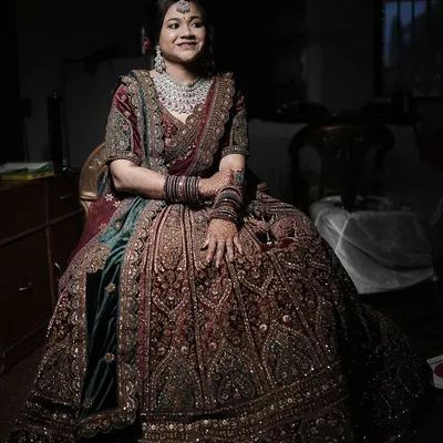 A stunning full-length portrait of a North Indian bride in her magnificent, heavily embroidered lehenga. The low-light setting adds a touch of drama and elegance.