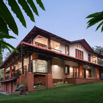The Varadarajan House in Coorg, seen from a low angle, shows how the structure is built into the hillside. The design features a prominent laterite stone base and extended eaves that provide shelter, creating a home that is both protected from and open to the elements.