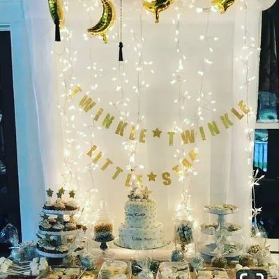 A complete 'Twinkle Twinkle Little Star' setup centered around the dessert table. The backdrop combines a wall of fairy lights with a glittery gold banner and foil balloons, creating a magical focal point for the celebration.