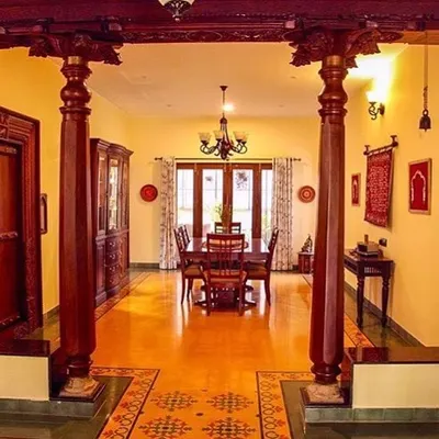 The dining space in the Roopa Hariprasad Residence is framed by two magnificent, hand-carved wooden pillars, a direct nod to traditional South Indian architecture. These structural elements define the space and serve as powerful sculptural forms.