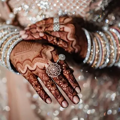 A close up of the bride's hands, showcasing her stunning rings and bracelets against the intricate mehndi. The sparkling details of her outfit create a beautiful, glittering backdrop.