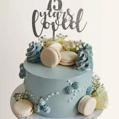 A beautiful and elegant cake to celebrate a 75th birthday. This design features a soft blue whipped cream finish, delicate silver details, and is adorned with fresh flowers and macarons.
