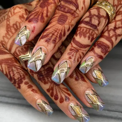 This intricate design features multi-tonal chrome with geometric gold outlines on long coffin nails. The way the colors shift makes this set captivating from every angle, especially against the henna.