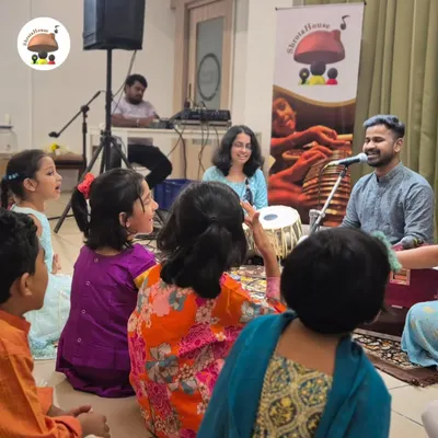 An interactive session in full swing. Our students gather around to learn from a visiting artist, absorbing the rhythms of the harmonium and tabla in a fun, group setting.