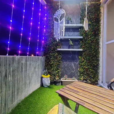 We transformed this balcony into a cozy evening retreat. Artificial turf on the floor, green walls for privacy, and soft curtain lights create a magical ambiance, perfect for relaxing after a long day.