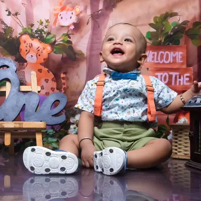 A joyful first birthday photoshoot with a jungle theme. The 'ONE' sign and happy expression make this a perfect milestone memory.
