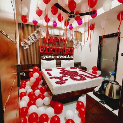 This 'Sweet 16' birthday decoration uses a classic red and white color scheme. The room is filled with balloons on the floor and ceiling, with 'HAPPY BIRTHDAY' foil letters and a bed covered in a rose petal heart design.