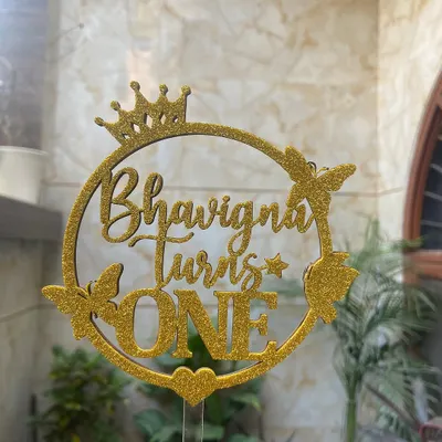This glittery gold topper for "Bhavigna Turns ONE" is all about sparkle and celebration. The design incorporates a crown and butterflies for a truly royal and whimsical first birthday theme.