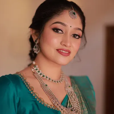This is my signature radiant bridal look. I focused on creating flawless, glowing skin with a classic winged eyeliner and a bold red lip, which perfectly complements the client's beautiful teal and gold Kanjivaram saree.