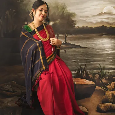 A stunning maternity portrait inspired by classical Indian art. The expectant mother sits by a painted river scene, holding a feather, creating a look of serene elegance.