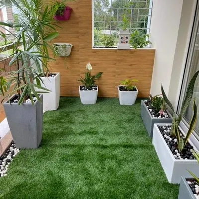 A modern balcony makeover featuring a lush artificial lawn bordered by decorative pebbles. We used sleek, minimalist planters and a wood-paneled accent wall to create a clean and contemporary green space.