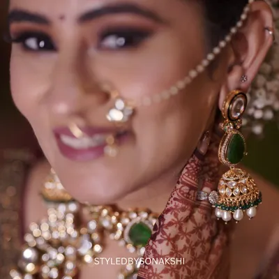 A close-up on the exquisite details of a bridal look. This shot highlights the beautiful kundan and emerald jhumkas and the delicate nath, which add a touch of tradition and color to the bride's ensemble.