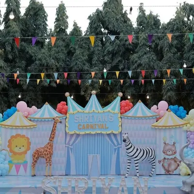 The main stage for a pastel carnival themed first birthday. This outdoor setup features a backdrop designed like circus tents with cute animal characters.