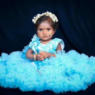 A little princess in her fluffy blue dress against a simple black backdrop. This high-contrast studio shot makes the vibrant color of her outfit pop, creating a dramatic and beautiful portrait.