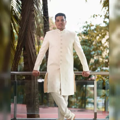 A stylish, full-length portrait of the groom in his elegant off-white sherwani. His relaxed yet confident pose on the balcony makes for a great shot.