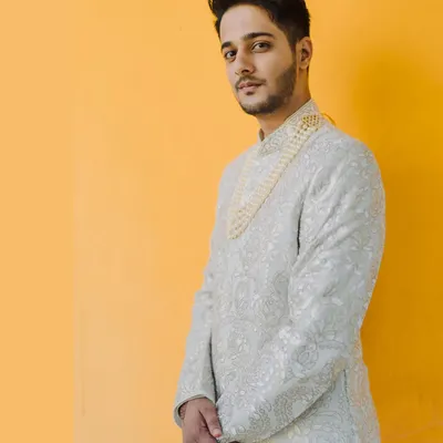 A stylish portrait of the groom against a vibrant yellow wall. His elegant sherwani and confident pose make for a striking and modern groom portrait.