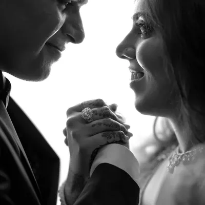 A powerful black and white close-up focusing on the couple's hands and expressions. The high contrast and backlighting create a dramatic and intimate portrait, highlighting the engagement ring and their connection.