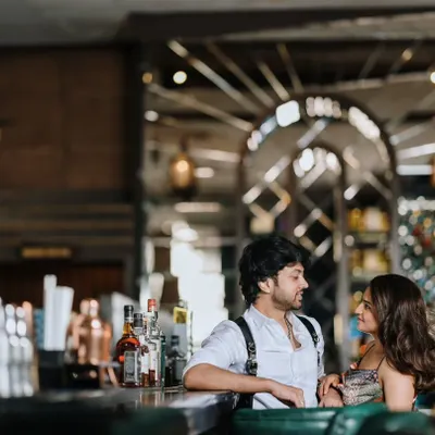 A stylish pre-wedding shoot in a sophisticated bar. The couple shares a conversation at the counter, creating a candid and modern urban love story.