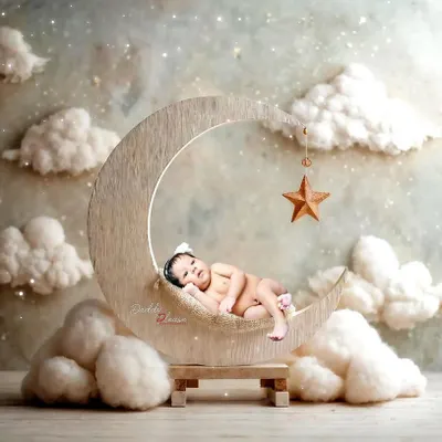 A peaceful newborn portrait featuring a baby sleeping on a wooden crescent moon prop, surrounded by soft, dreamy clouds. These sessions are designed to be calm and safe for your little one.