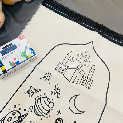 A closer look at the "Colour, Create, Pray" prayer mat for kids. The design features the Kaaba, planets, and stars, ready to be colored in with the included fabric markers, making prayer time a creative and engaging experience.