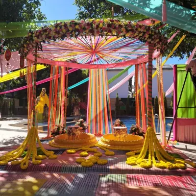 A poolside Haldi setup in Jim Corbett, combining colorful ribbon drapes with traditional marigold garlands. The low seating (patlas) and floral arch create a perfect space for the ceremony.