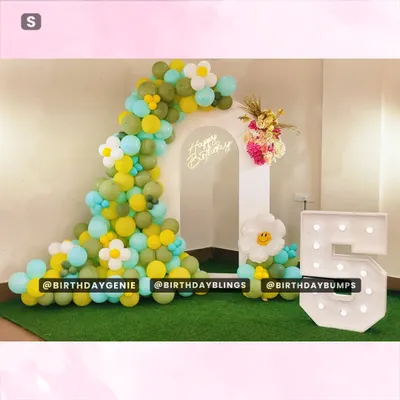 A cheerful and simple birthday setup with a daisy-flower balloon arch in green and yellow, a neon sign, and a light-up number '5'.