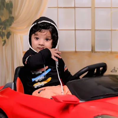 A close-up of our little driver, looking cool and confident in his ride. The black hoodie adds a stylish touch to this 6-month-old's car-themed photoshoot.