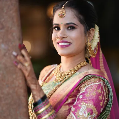 A radiant close-up of a South Indian bride, showcasing her beautiful smile, intricate gold jewelry, and the detailed embroidery on her wedding saree.