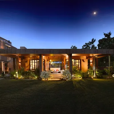 The K Pavilion, illuminated at night, serves as the heart of the garden. This outdoor lounge binds the existing home to the landscape, creating a warm and inviting central hub for family life that is completely open to the elements.