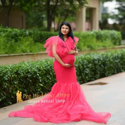 This vibrant red mermaid gown features a ruffled neckline and a sheer tulle train, creating a bold and stylish look. It's perfect for an outdoor maternity shoot in a modern park or garden setting.