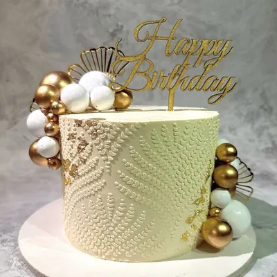 An example of detailed buttercream work. This cake features an intricate white-on-white stenciled pattern, accented with clusters of gold and white spheres for a sophisticated finish.