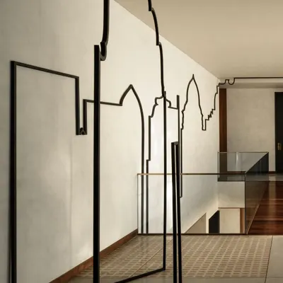 A closer view of the "Continuous Fragments" installation, where the black metal line travels from a wall-mounted piece to a freestanding element, blurring the line between two-dimensional drawing and three-dimensional sculpture.