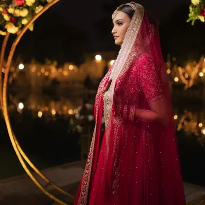 A breathtaking bridal portrait against a backdrop of golden lights. The bride's elegant profile and the beautiful red of her lehenga create a dramatic and timeless image.