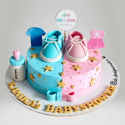 A "He or She" gender reveal cake designed as a heart. One side is blue for a boy and the other is pink for a girl, topped with adorable baby shoes and clothes.