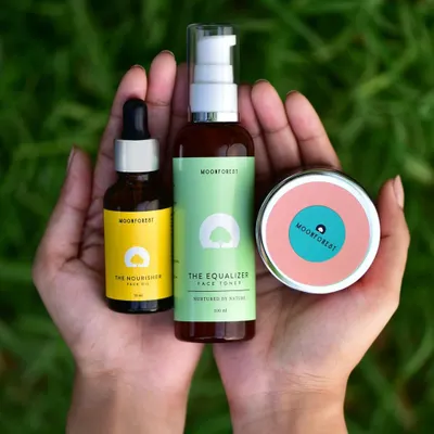 A lifestyle shot showing the Moon Forest skincare line held in hands against a natural green background. This connects the products to nature and personal care.