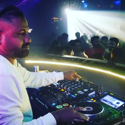 A side profile shot of me at the decks at Cavalry Lounge, with the crowd visible in the background. The spotlight catches the intensity and focus required to manage the music and the room.