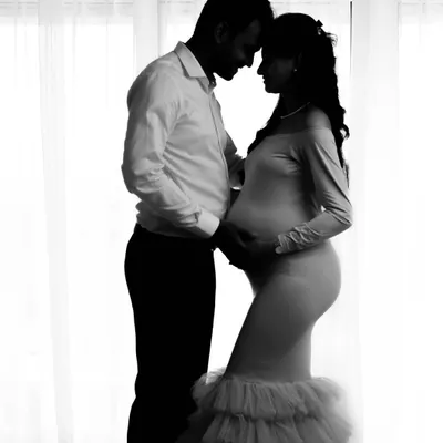 A stunning black and white silhouette of an expecting couple against a bright window. This technique creates a dramatic, intimate, and timeless maternity portrait.