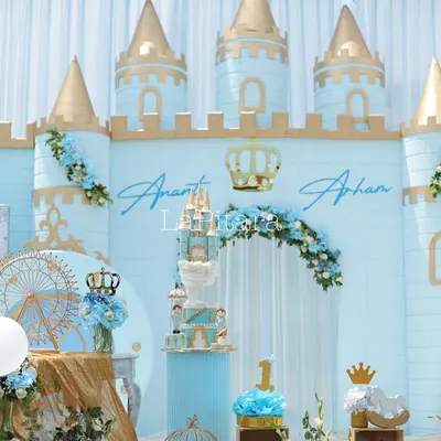 The main stage of a royal prince-themed birthday, featuring a magnificent castle backdrop in pastel blue and gold. The setup includes a tiered cake display, personalized names, and floral arrangements, creating a picture-perfect focal point for the celebration.
