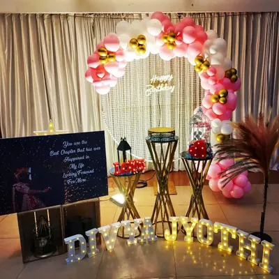 A beautiful birthday surprise for Divya Jyothi. The setup features a pink and gold balloon arch, a personalized poster with a romantic quote, and light-up letters spelling her name.