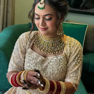 A dreamy bridal look featuring a soft, romantic updo with delicate twists and face-framing tendrils. This hairstyle perfectly complements her intricate lehenga and jewelry.