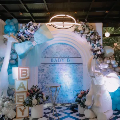 A stunning Dior-inspired baby shower stage in cool shades of blue, white, and silver. The setup includes a large elephant prop, 'BABY' blocks, and a beautiful floral and balloon arch over a custom backdrop.