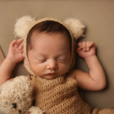 A close-up of a sleeping newborn dressed as a tiny bear, complete with a matching teddy. This pose highlights the peacefulness of a newborn, perfect for a classic infant portrait.