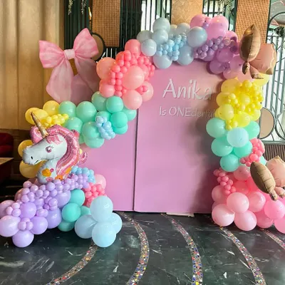 A magical unicorn-themed first birthday for Anika, featuring a "ONEderful" backdrop in pink. The setup is framed by a whimsical pastel rainbow balloon arch and includes a cute unicorn foil balloon, creating a perfect fairytale setting.