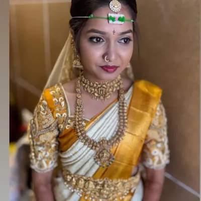 A classic South Indian bridal look, featuring a sharp wing liner and a bold lip that perfectly matches the bride's white and gold Kanjivaram saree. The look is completed with traditional temple jewelry and a matha patti.