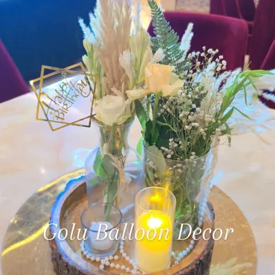 An elegant boho-style table centerpiece featuring fresh flowers, pampas grass, and candles on a rustic wooden platter.