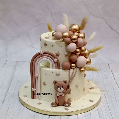 A sophisticated two-tier teddy bear cake for a baby celebration. This 2kg chocolate cake features a fondant teddy holding a cascade of pink and gold decorative balloons.