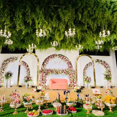 A stunning reception stage featuring a ceiling of lush greenery and dozens of hanging crystal chandeliers. This design creates an immersive, enchanted forest ambiance for an unforgettable evening.